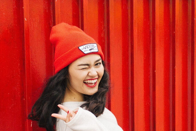 Woman in a red hat and white sweater smiles giving the peace sign