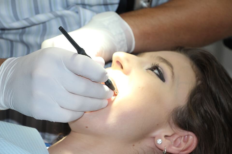 A woman in makeup receives cosmetic dentistry from a dentist.