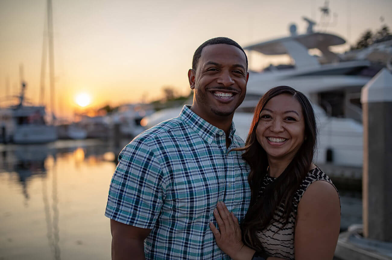 Couple stands at marina embracing and smiling